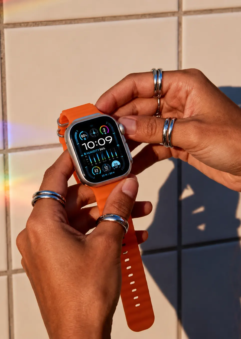 Hands fastening an Aurelius Chronograph with orange ocean band in warm sunlight